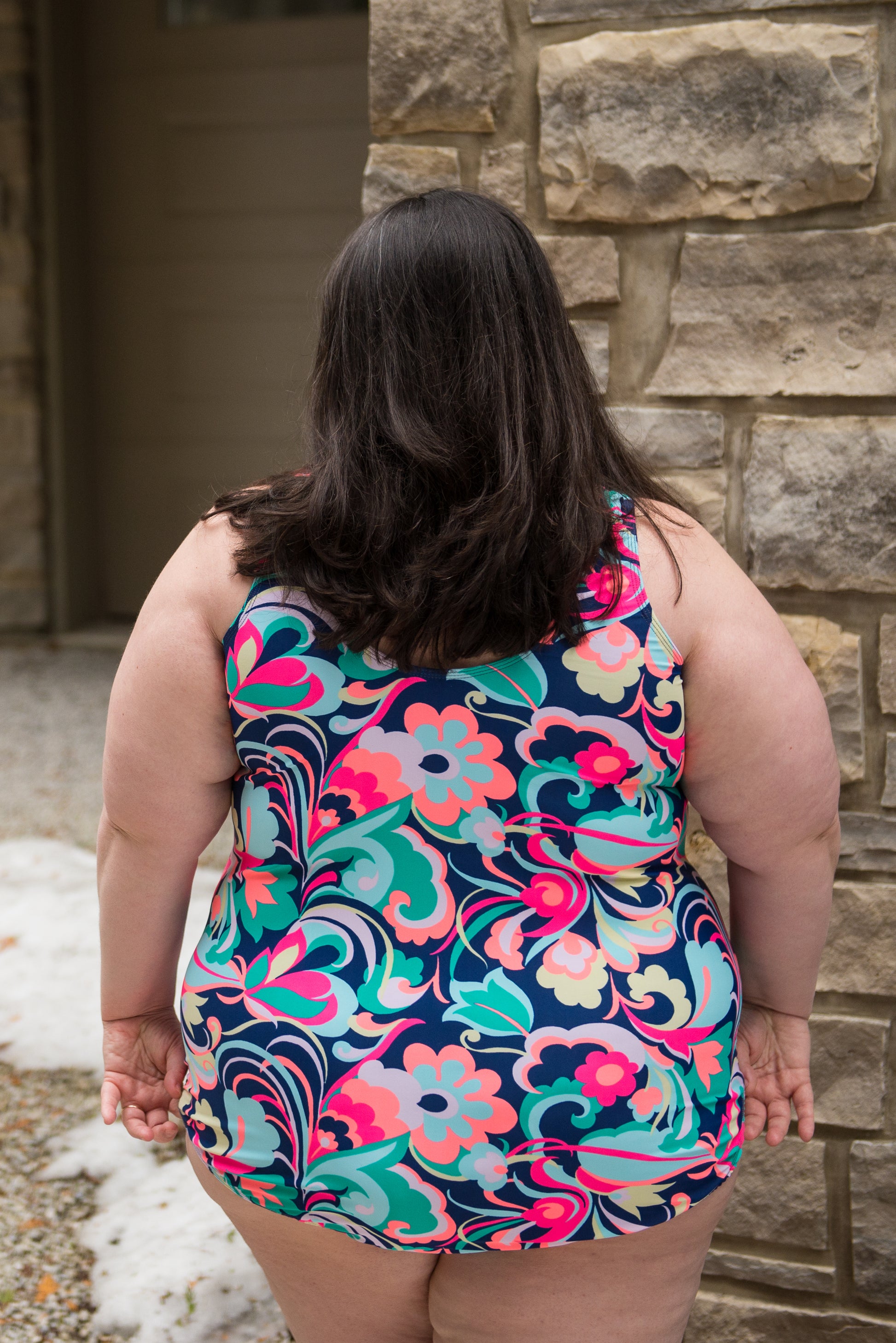 Photo of back view of plus size woman wearing floral & paisley DIBY Club Amelia one-piece swimsuit