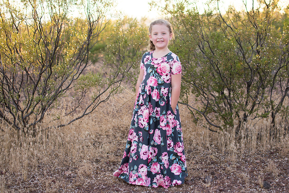 A young girl is wearing the Samantha Dress with short sleeves and a maxi length. Features a floral pattern. 