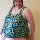 Plus size woman sitting on a stool wearing a green, blue, and black DIBY Club Amelia One-piece swimsuit with leopard print pattern.