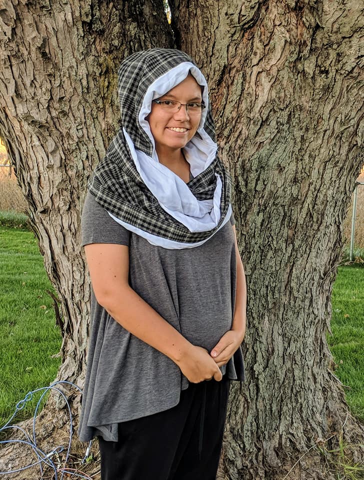 Hooded infinity scarf pattern tester. Hood is up. Features a black plaid pattern for the main fabric and a light gray lining. 