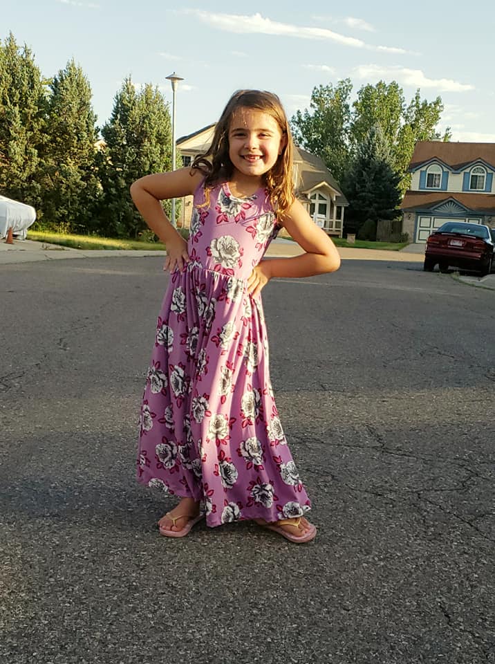 A young girl displays a sleeveless, floral themed, maxi-length Samantha Dress. 