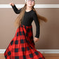 A young girl is wearing the Samantha gathered dress pattern with long sleeves and maxi length. The top is black and the bottom is a red and black gingham pattern. 